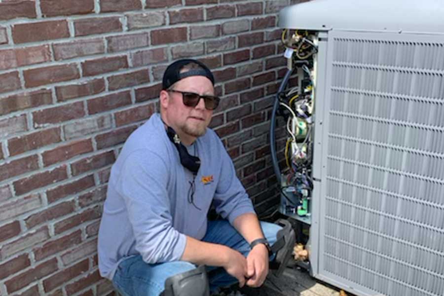 HVAC technician kneeling next to an open outdoor air conditioning unit.