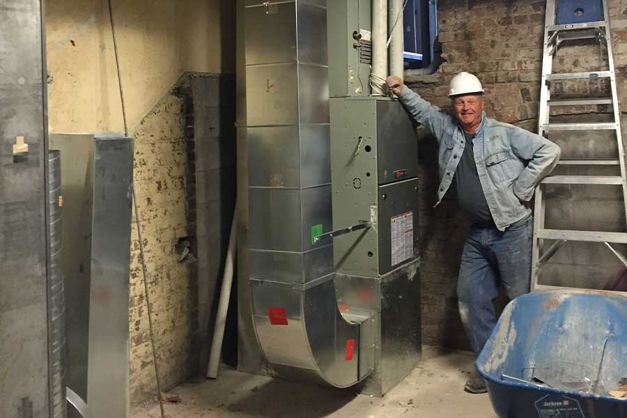 A worker in a hard hat standing next to an HVAC system